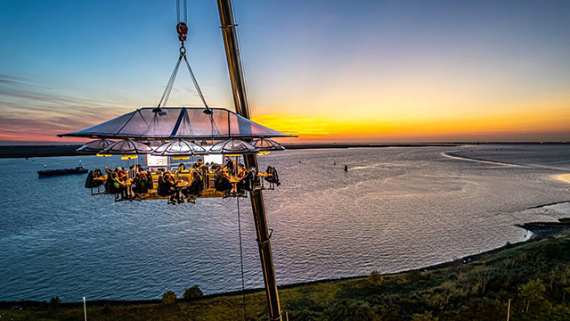 Dinner in the Sky platform suspended by a crane above the waterfront at sunset